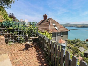 Ein Haus mit Ziegelterrasse, Holzzaun und Blick auf einen See.