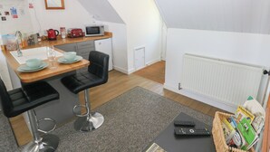 A compact kitchen with a dining area, including a table with chairs, a microwave, a kettle, and a refrigerator. - Seaside Steps (Goodwick)