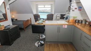 A compact kitchen with a dining area, a small bedroom, and a view of the sea. - Seaside Steps (Goodwick)