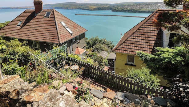 A coastal property with two houses, a stone wall, and a view of the sea and distant hills. - Seaside Steps (Goodwick)