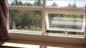 Ein Zimmer mit Schreibtisch und zwei Stühlen, ein großes Fenster mit Blick auf einen See und Berge, und ein Vorhang auf der linken Seite.