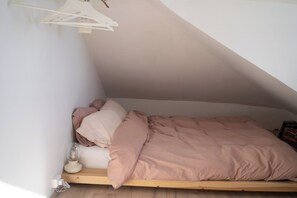 A single bed in a loft-style room with a sloped ceiling, a bedside table with a lamp, and a wall-mounted shelf. - A Historic Icelandic Lakeside Home, where nature and people reconnect (Selfoss)