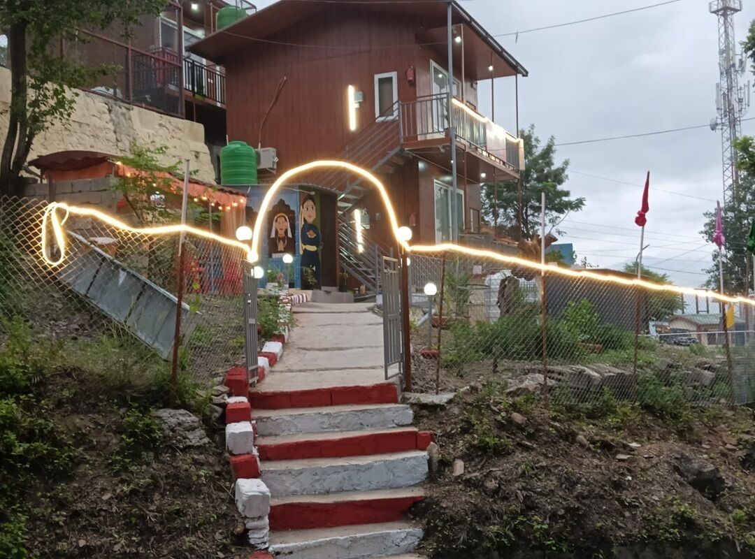 Um edifício com escadaria que leva a uma porta, cercado por uma grade e vegetação.