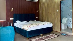 Ein Schlafzimmer mit einem Bett, einem Deckenventilator, einer Klimaanlage, einem Badezimmer mit Dusche und einem blauen Stuhl.