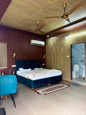 A bedroom with a bed, a ceiling fan, an air conditioning unit, a bathroom with a shower, and a blue chair.