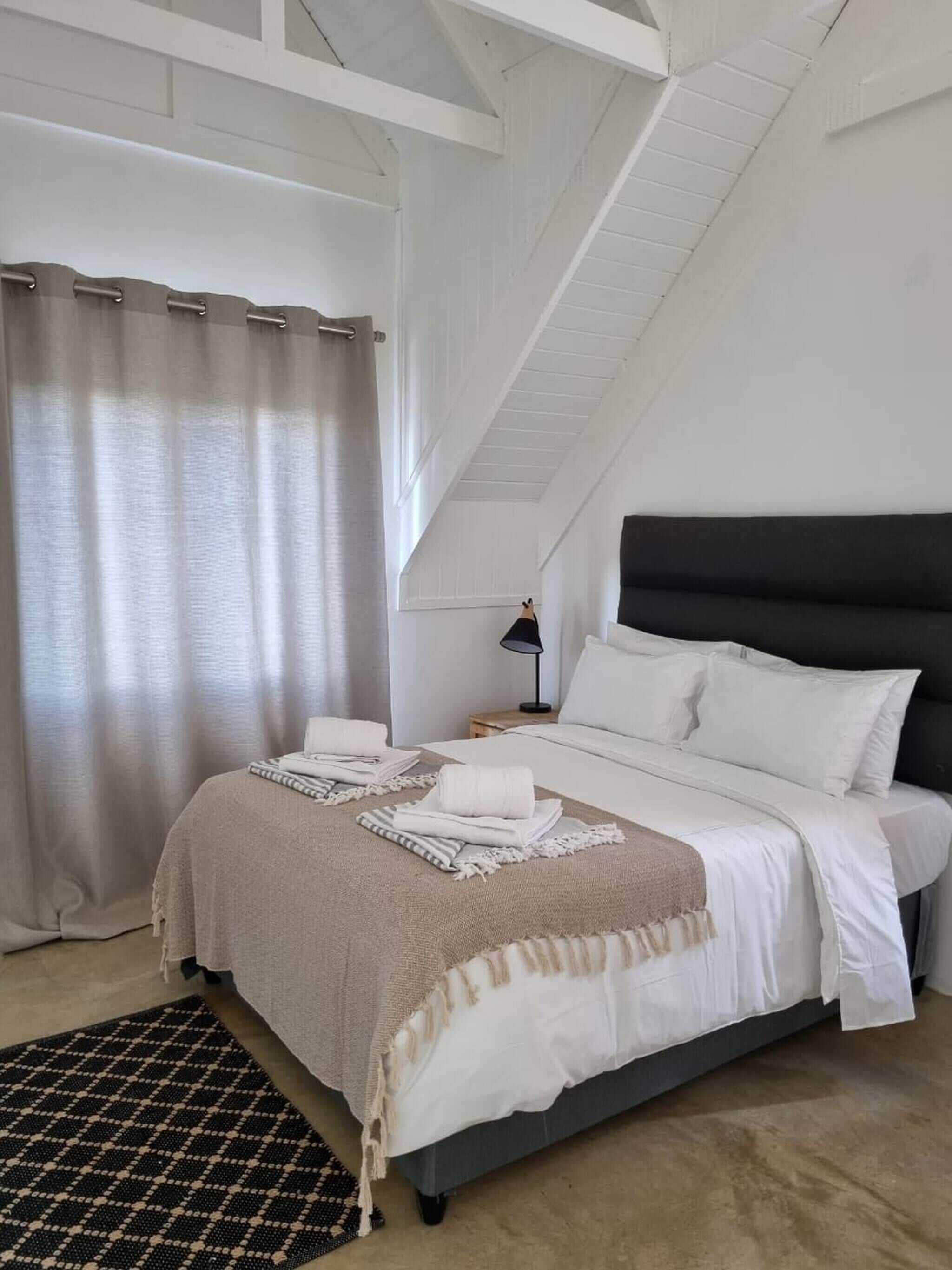 A bedroom with a bed, a nightstand, a lamp, and a window with curtains.