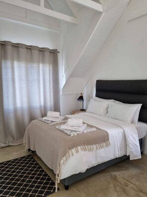 A bedroom with a bed, a nightstand, a lamp, and a window with curtains.