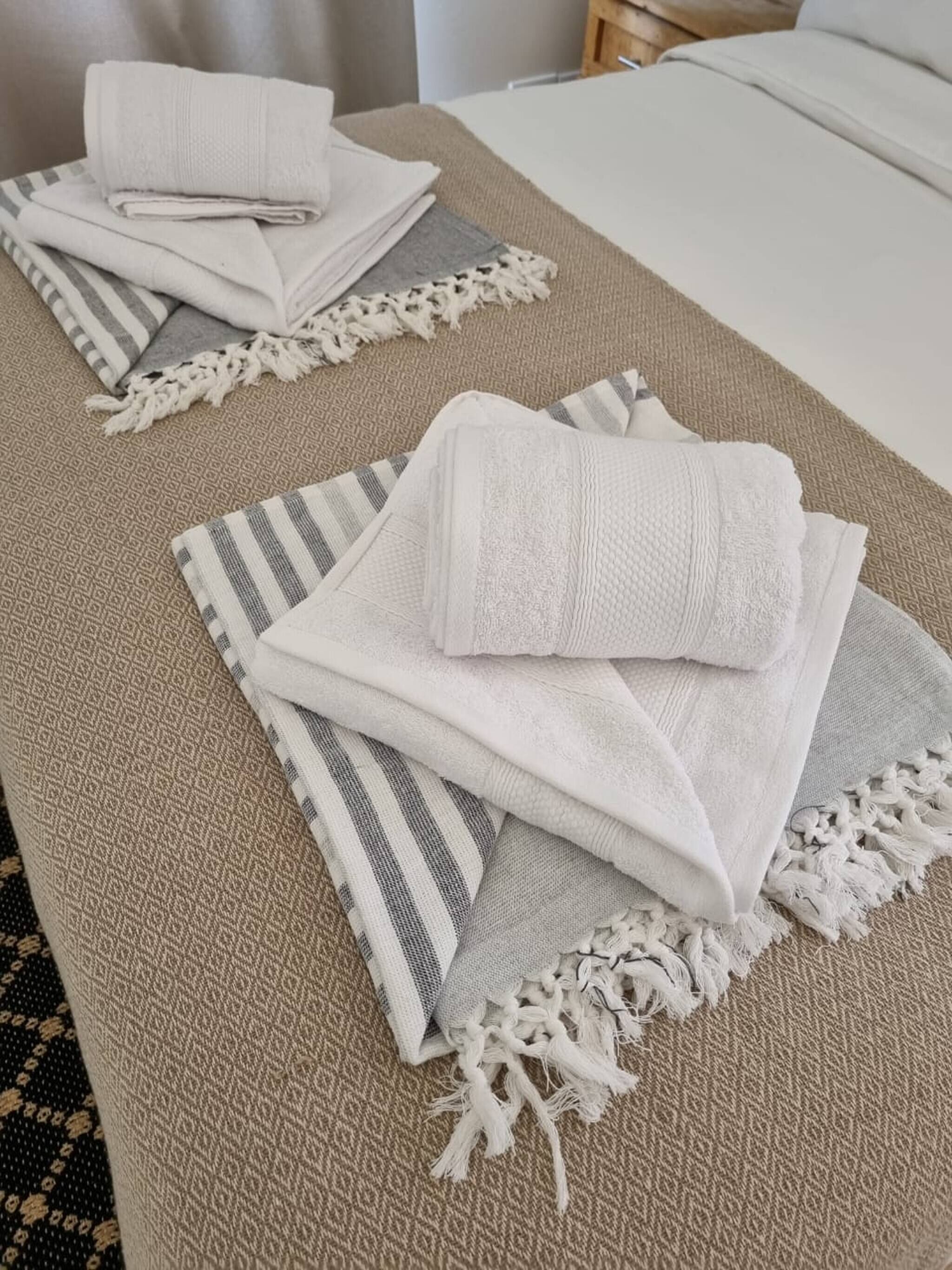 A neatly arranged bed with a white comforter, a striped pillow, and a beige throw blanket with fringe.