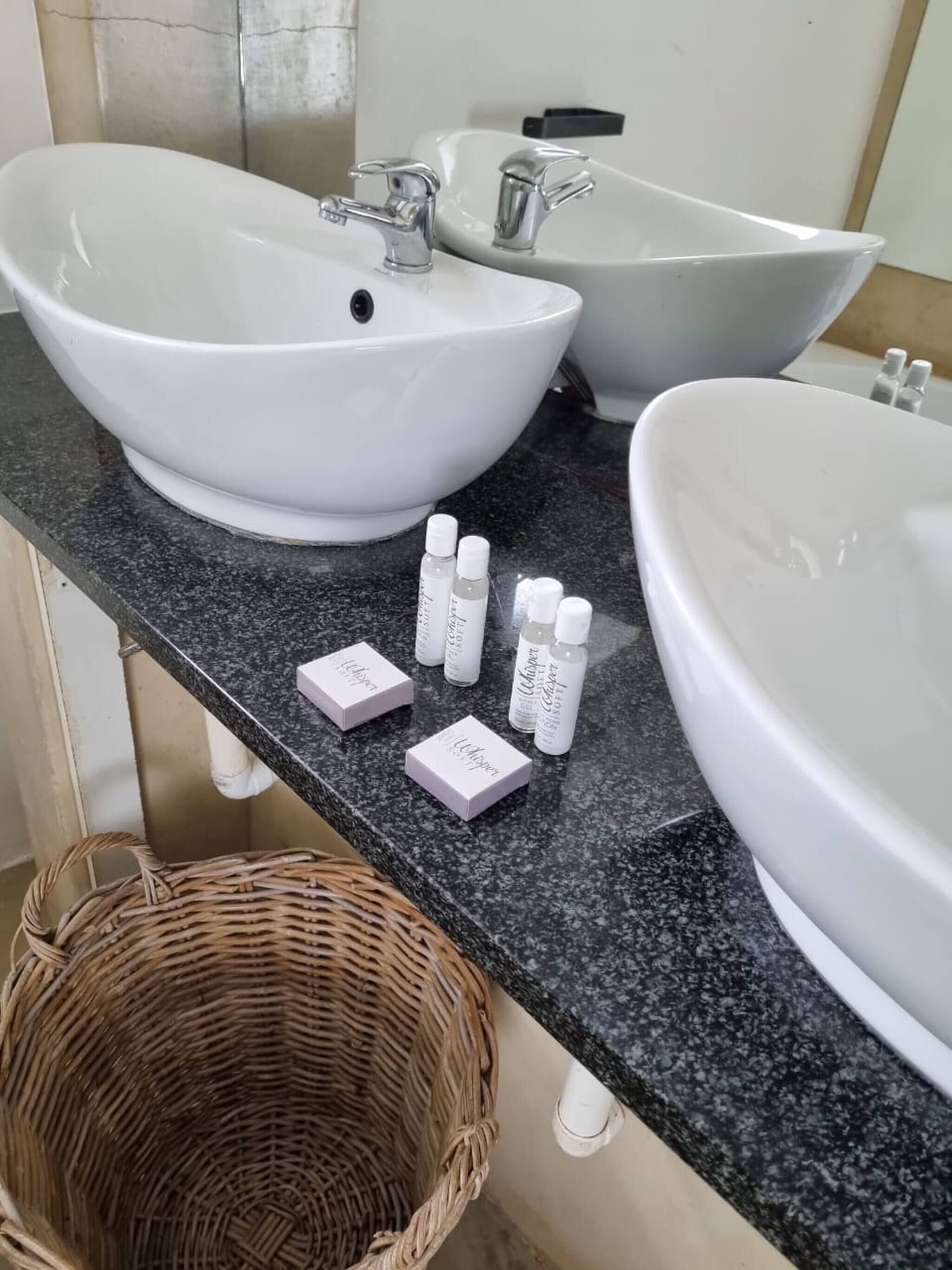 A bathroom with two large white sinks, a mirror, and a wicker basket on the counter.