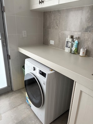 A laundry area with a washing machine, a countertop with bottles, and a door to a laundry room.