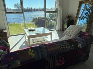 A living room with a sofa, a glass coffee table, and a view of a lake. - Stylish Waterfront home (Helensvale)