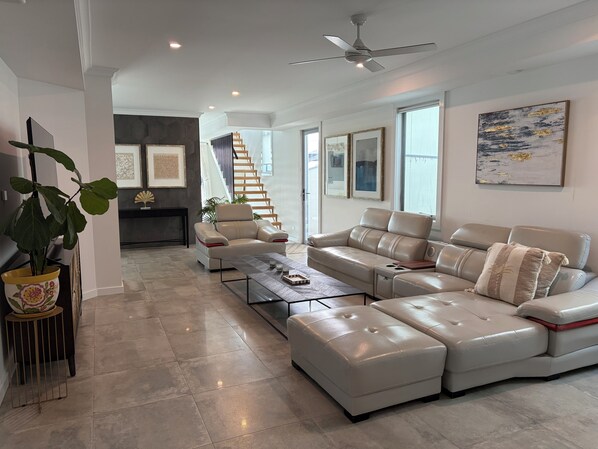 A modern living room with a sectional sofa, a coffee table, and a staircase leading to an upper floor.