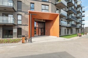 A modern building with a wooden entrance canopy, glass balconies, and a paved driveway. - Nadmotławie C43 | Riverside | Sauna & Gym (Gdańsk)