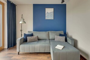 A modern living room with a grey sofa, a blue accent wall, and a floor lamp. - Nadmotławie C43 | Riverside | Sauna & Gym (Gdańsk)