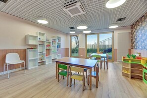 A children's playroom with a wooden table, chairs, shelves with toys, and a view through the door. - Nadmotławie C43 | Riverside | Sauna & Gym (Gdańsk)