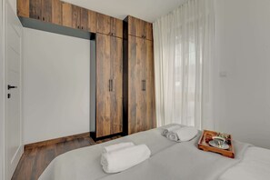 A bedroom with a bed, a wooden wardrobe, and a tray with a croissant and flowers. - Nadmotławie C43 | Riverside | Sauna & Gym (Gdańsk)