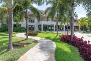 A landscaped area with palm trees, a curved pathway, and a building with large windows and outdoor seating. - BeachClass EcoLife Porto de Galinhas (Ipojuca)