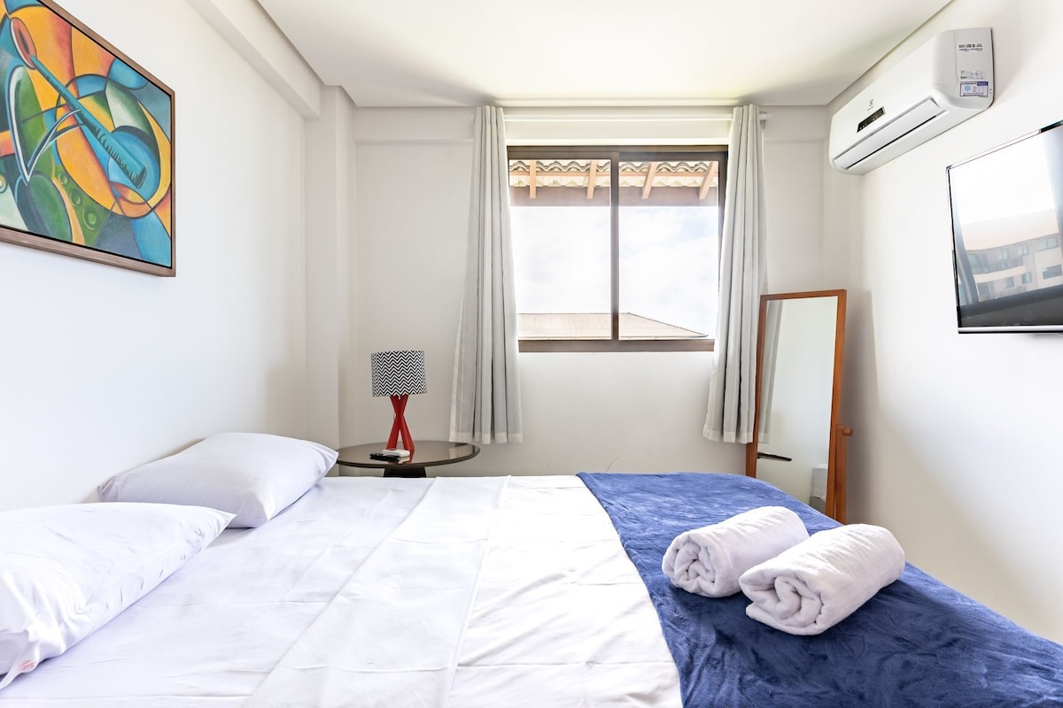 Ein Hotelzimmer mit einem Bett, einer Lampe, einem Fenster, einer Klimaanlage und einem Bild an der Wand.