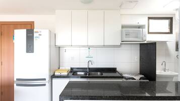 Cozinha moderna com armários brancos, pia de aço inoxidável, micro-ondas e geladeira.