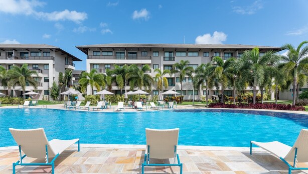 Ein Pool mit Liegestühlen und Sonnenschirmen, umgeben von Palmen und einem Hotelgebäude.