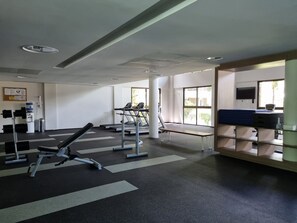 Uma academia com equipamentos de exercícios, bebedouro e mesa com computador.