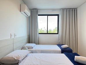 Quarto de hotel com duas camas, uma janela com cortinas, ar condicionado e vista para áreas verdes.