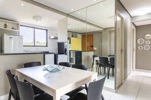 A modern kitchen with a refrigerator, a window, and a dining area with a table and chairs. - BeachClass EcoLife Porto de Galinhas (Ipojuca)