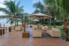 A wooden deck with wicker furniture and umbrellas, overlooking a beach. - BeachClass EcoLife Porto de Galinhas (Ipojuca)