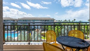 Ein Balkon mit Blick auf einen Swimmingpool, ein Gebäude im Hintergrund und zwei gelbe Stühle.