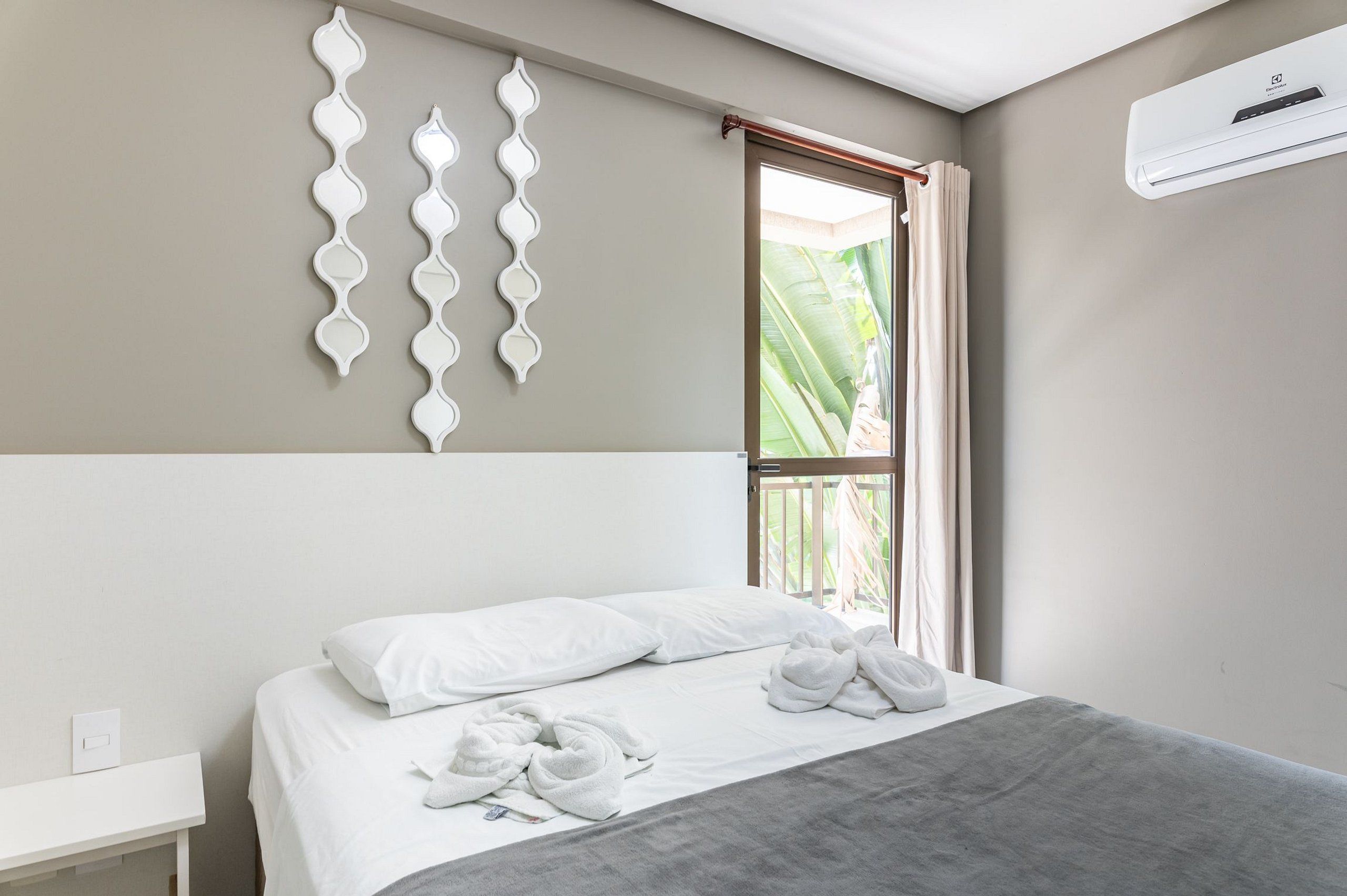 Quarto de hotel com cama, mesa de cabeceira, ar condicionado fixado na parede e janela com cortinas.