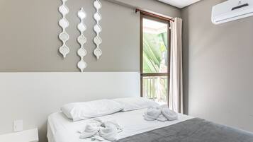 Quarto de hotel com cama, mesa de cabeceira, ar condicionado fixado na parede e janela com cortinas.