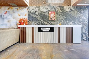 Bancada de recepção com parede de mármore, um quadro emoldurado e uma placa com a inscrição 'PALETTE Company-Serviced'.