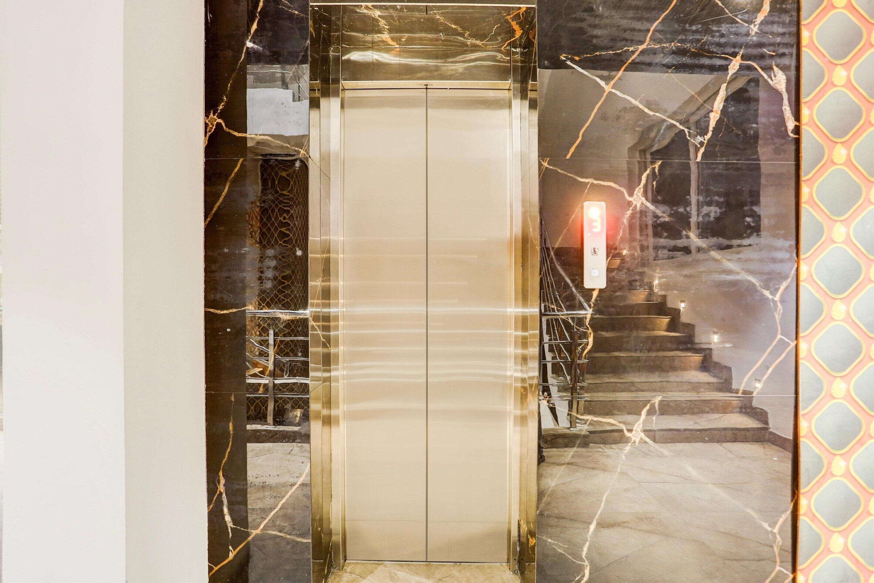 An elevator with a marble wall design and a staircase with a patterned wall to the right.