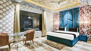 Ein modernes Schlafzimmer mit einem Glastisch, einem Bett mit blauer Kopfteil und Wandverkleidung mit Muster.