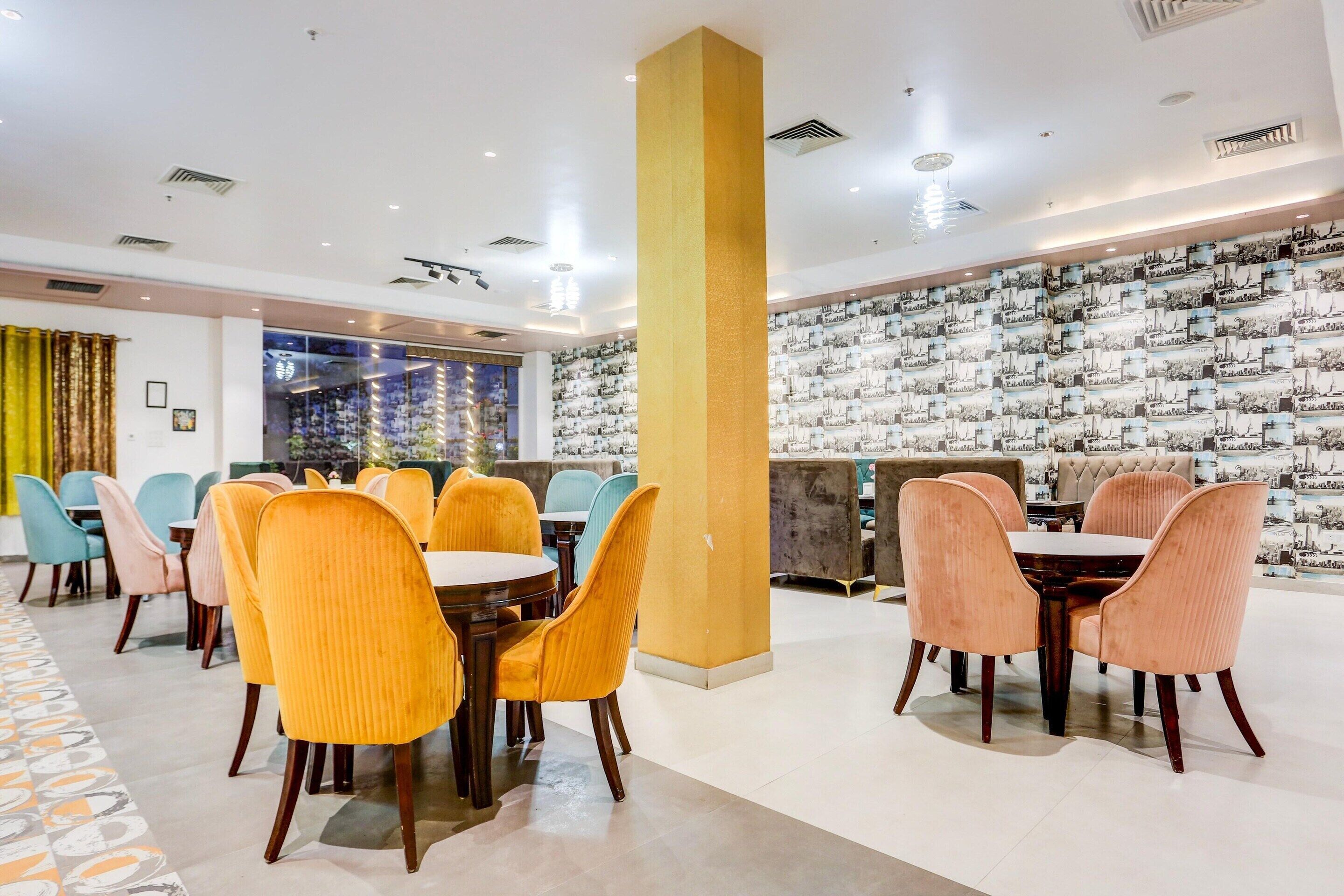 Une salle à manger d'hôtel avec des tables et des chaises rondes, un mur décoré de motifs et une grande colonne.
