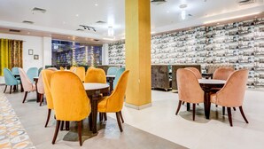 Ein Restaurantbereich in einem Hotel mit runden Tischen und Stühlen, einer Wand mit Muster und einer großen Säule.