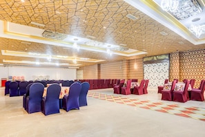 Uma sala de banquetes com teto de padrão geométrico, fileiras de mesas com cadeiras e piso estampado.