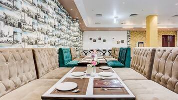Un comedor con una mesa larga dispuesta para una comida, sillas tapizadas y una pared con fotografías del paisaje urbano.