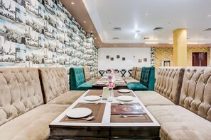 Un comedor con una mesa larga dispuesta para una comida, sillas tapizadas y una pared con fotografías del paisaje urbano.