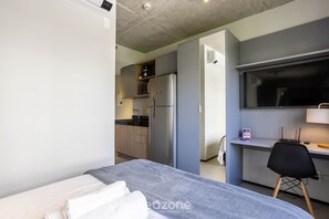Ein modernes Hotelzimmer mit Bett, Schreibtisch, Kühlschrank und einer Küchenzeile.