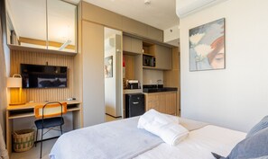 Ein Hotelzimmer mit Bett, Schreibtisch mit Stuhl, Fernseher, einer Küchenzeile und einem Bild an der Wand.