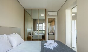 Ein modernes Hotelzimmer mit einem großen Bett, einem begehbaren Kleiderschrank, einem Badezimmer mit Waschbecken und Spiegel sowie Blick ins Freie.