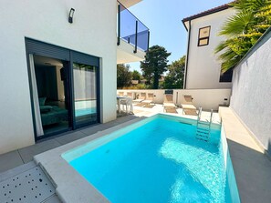 A swimming pool with a clear blue water, surrounded by a patio area with chairs and a table. - Villa Sorelle 1 & Sorelle 2 (Zaton)