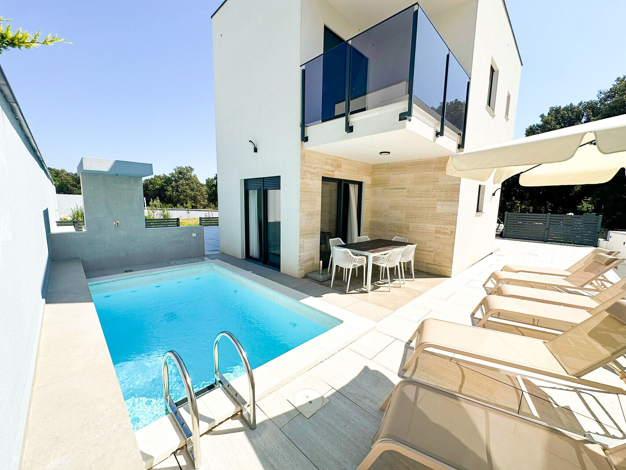 A modern outdoor pool area with a glass balustrade, lounge chairs, and a dining table.