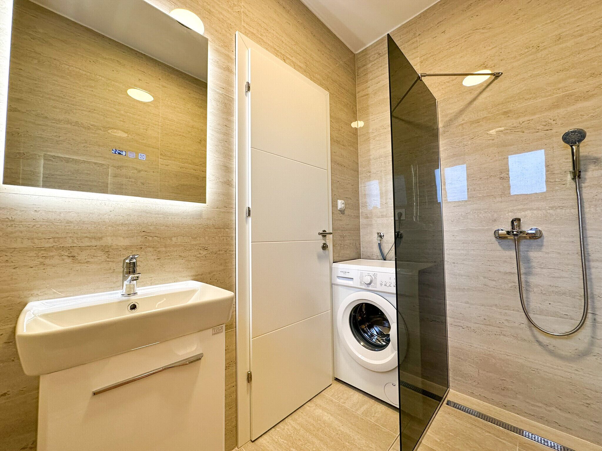 Ein modernes Badezimmer mit Waschbecken, Spiegel, Dusche und Waschmaschine.