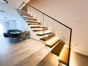 Eine moderne Treppe mit Glastrennläufen und Holzboden, die zu einem Essbereich mit Tisch und Stühlen führt.