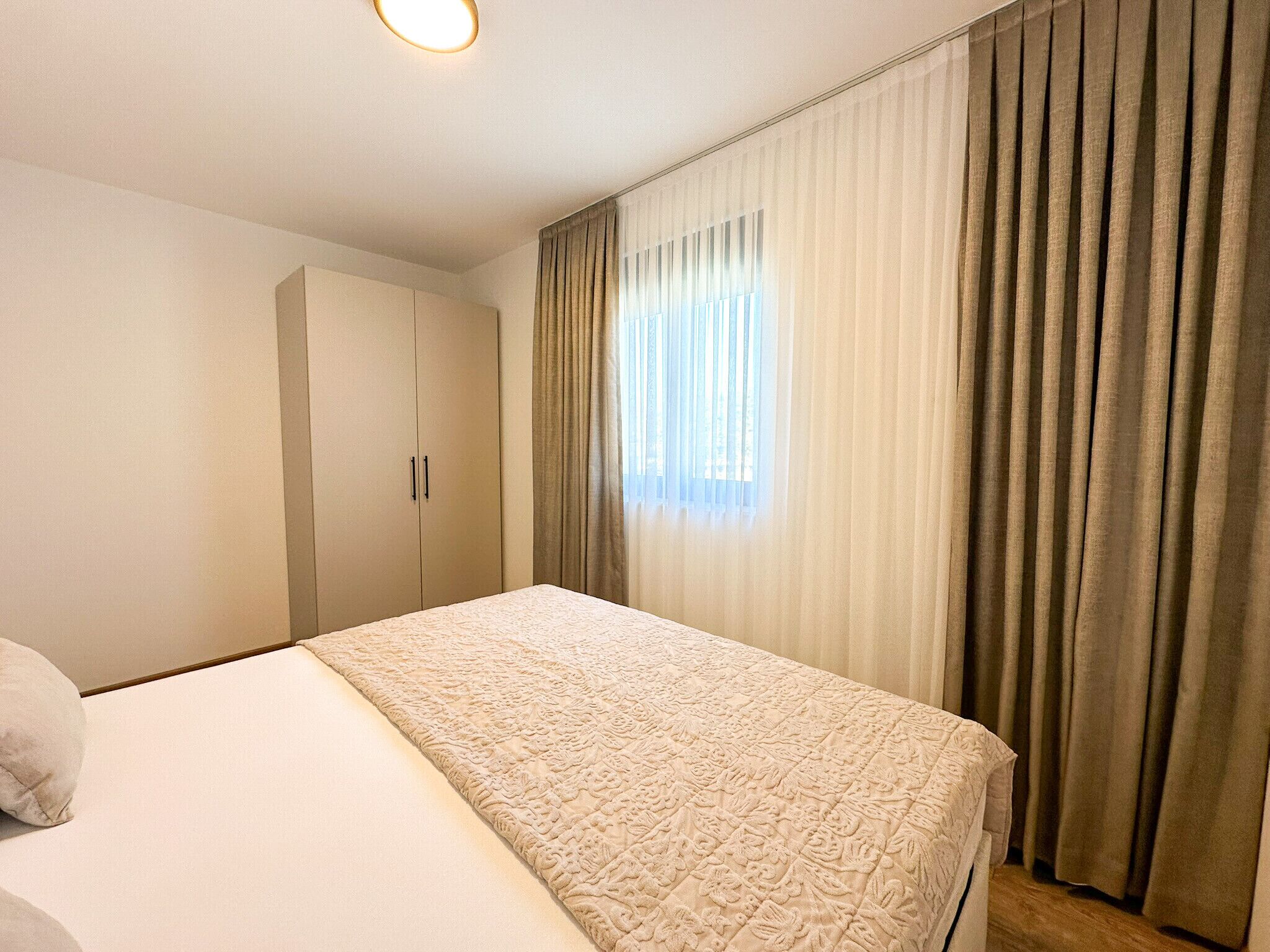 A hotel room with a bed, a wardrobe, and a window with curtains.