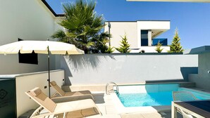 Uma área de piscina no terraço com espreguiçadeiras, piscina e um guarda-sol branco.