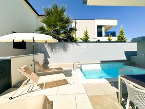 Ein Poolbereich auf dem Dach mit Liegestühlen, einem Pool und einem weißen Sonnenschirm.