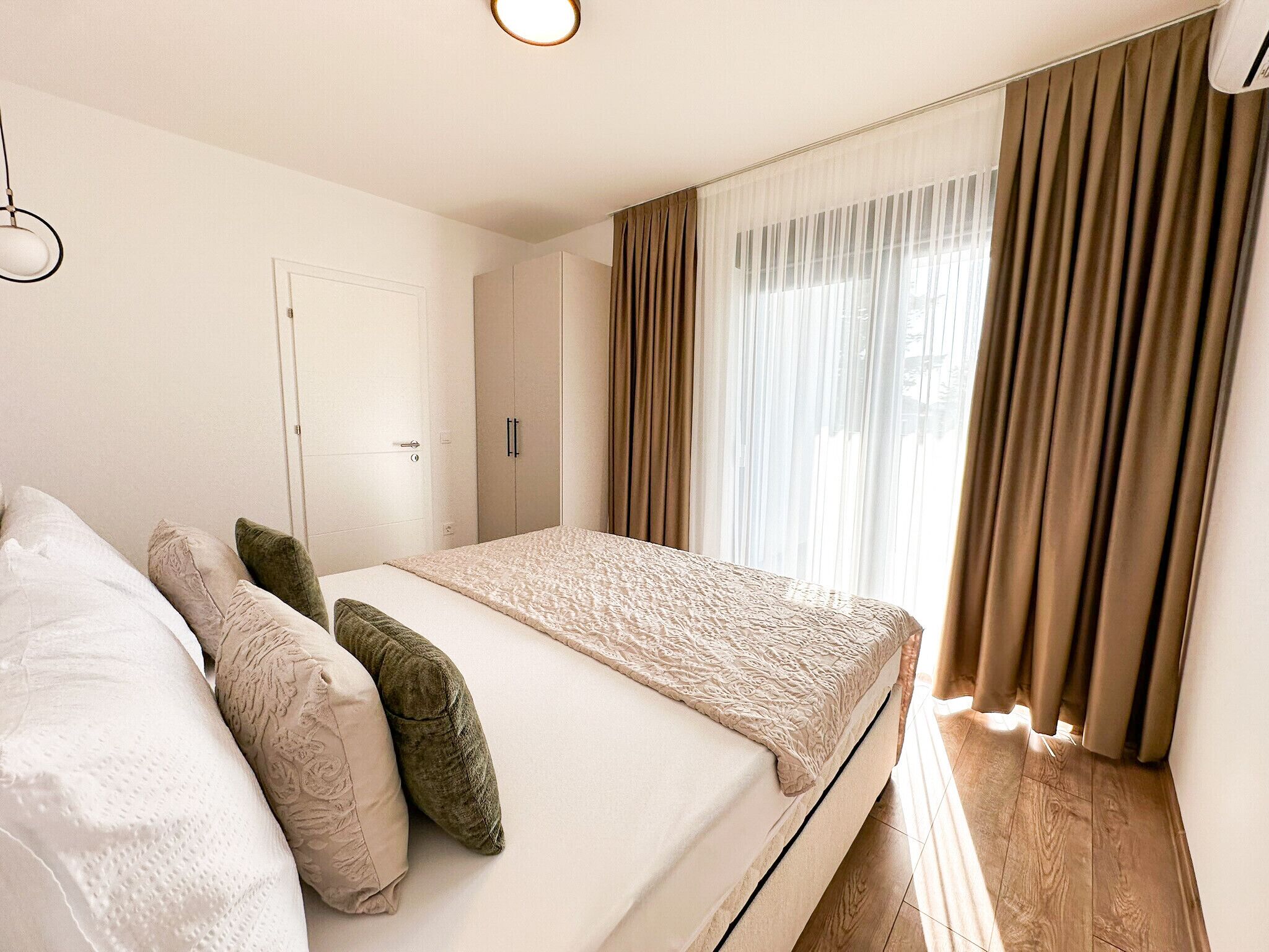 A bedroom with a bed, pillows, a door, and curtains.